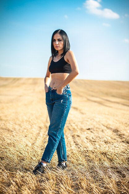 Modelo de mujer hermosa con ropa de algodón de verano posando en el campo de otoño con pila de heno