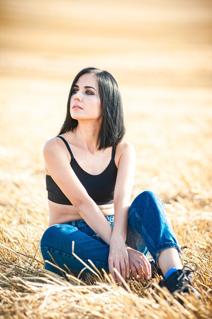 Modelo de mujer hermosa con ropa de algodón de verano posando en el campo de otoño con pila de heno