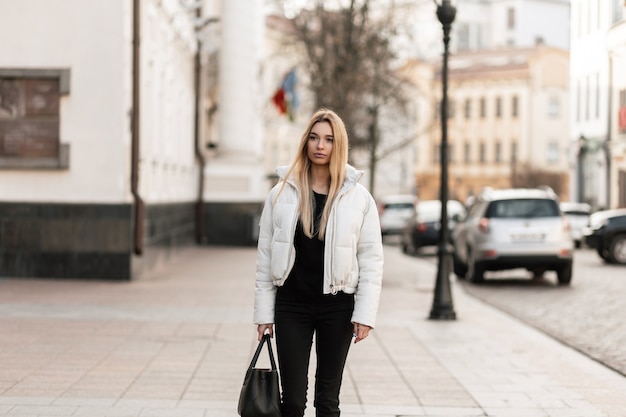 modelo de una mujer joven con una chaqueta blanca y un bolso de cuero de moda se encuentra en la calle