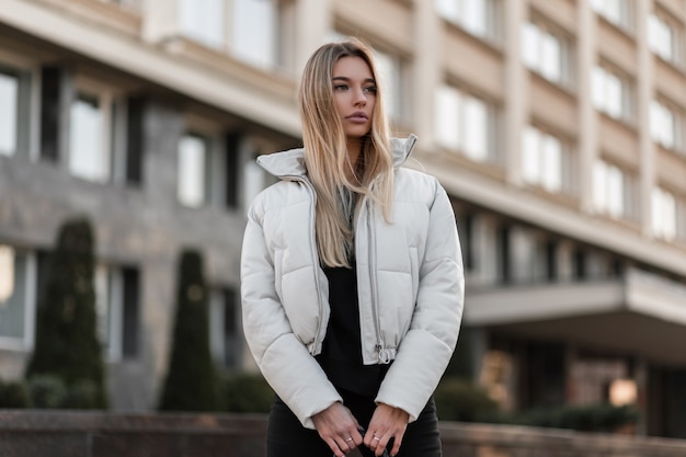 modelo de una mujer joven con una chaqueta blanca y un bolso de cuero de moda se encuentra en la ciudad