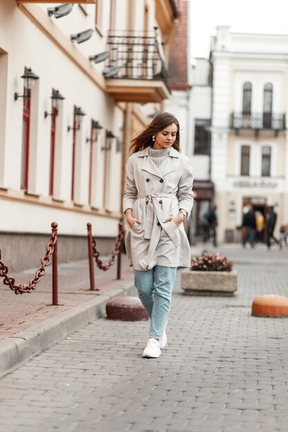 Foto modelo de una mujer joven con una gabardina y un suéter vintage de punto camina por la calle