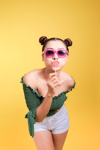 Modelo de mujer joven hermosa con estilo glamour con labios rojos con caramelo sobre fondo amarillo.