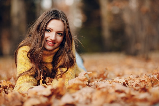 Modelo de mujer joven en el parque de otoño con hojas de arce de follaje amarillo. Moda de temporada de otoño.