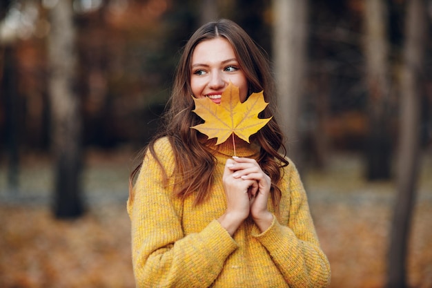 Foto modelo de mujer joven en el parque de otoño con hojas de arce de follaje amarillo moda de temporada de otoño