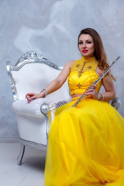 Modelo de mujer joven retrato en vestido amarillo etapa con flauta en las manos. Instrumento de viento en el flautista en el fondo de la pared con textura. Cartel para escuela de publicidad. Concepto de pieza musical o concierto.