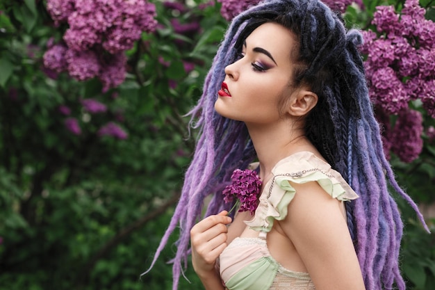 Modelo de mujer joven sexy con rastas de color en ropa interior está en las flores de color lila