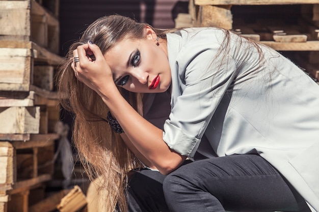 Modelo de mujer con maquillaje brillante y labios rojos en una chaqueta de moda en el fondo de cajas de madera