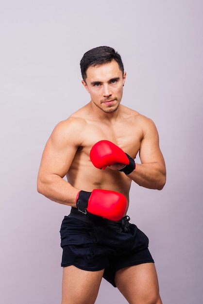 Modelo musculoso deportivo joven en guantes de boxeo sobre fondo gris macho flexionando sus músculos