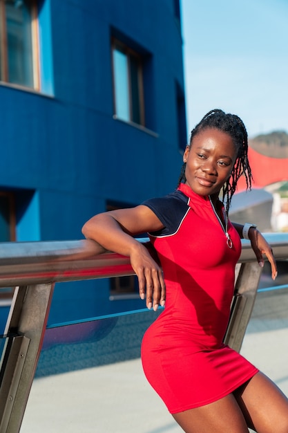 Modelo negro chica afro posando sonriente y divertido en la ciudad al atardecer con un vestido rojo y zapatillas blancas