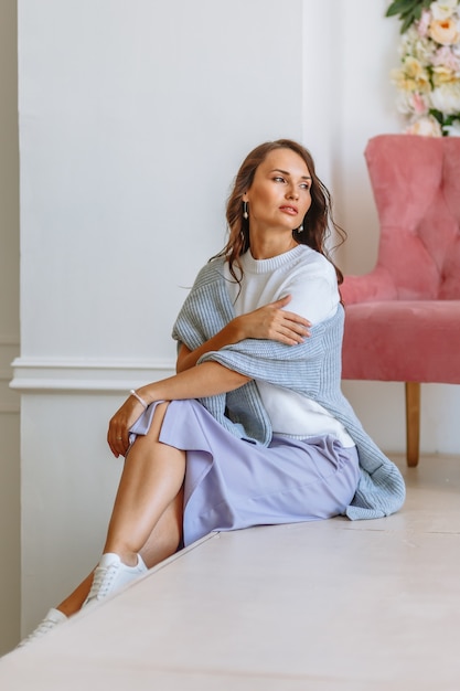 Modelo de niña con una chaqueta blanca y falda azul, muestra ropa mientras está sentado