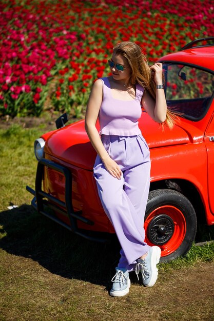 Una modelo de niña con ropa informal se sienta en un auto rojo entre campos de tulipanes