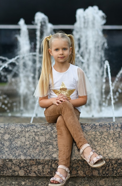 Modelo de niña sentada cerca de la fuente de la ciudad.