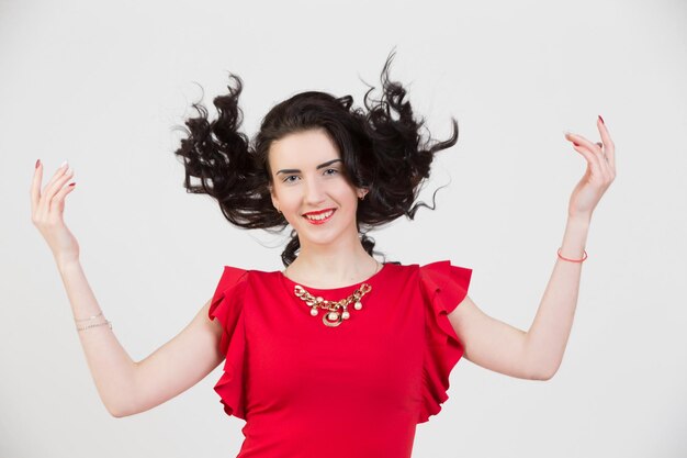 Una modelo de niña con un vestido rojo brillante con las manos en alto y el pelo rizado ondeando Morena brillante