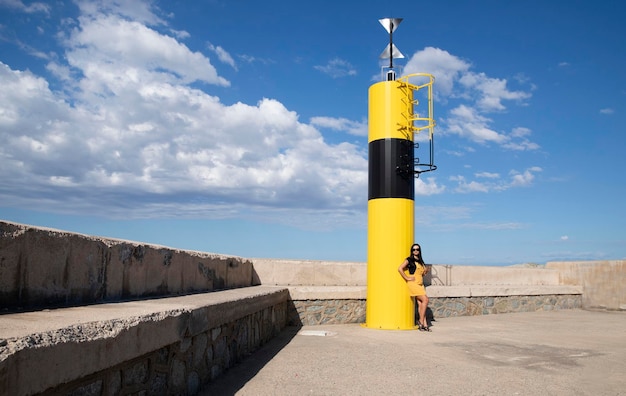 Modelo en overoles amarillos cerca del faro amarillo al aire libre