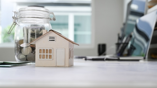Modelo para casa e potes de vidro com moedas colocando na mesa branca. Planejando economizar dinheiro para comprar uma casa ou um conceito de investimento imobiliário.
