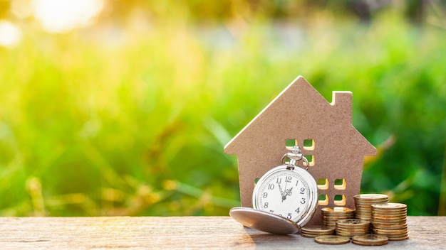 Modelo de pequeña casa y un reloj con pila de monedas de oro.