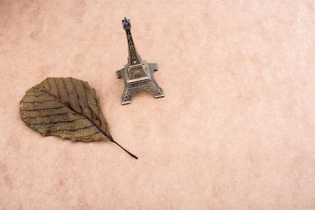 Modelo pequeno Torre Eiffel e uma folha seca em fundo marrom