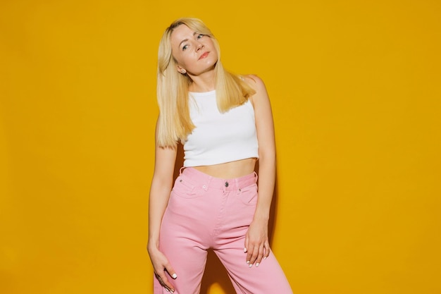 La modelo posa en el estudio sobre un fondo amarillo Una mujer joven con un top blanco y jeans rosas Traje hipster de moda