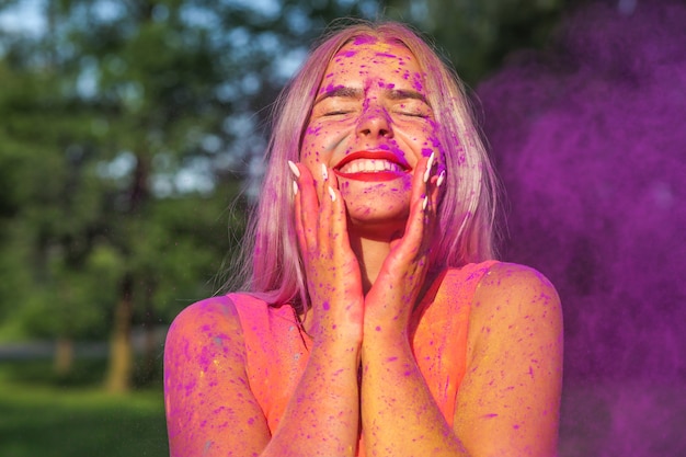 Foto modelo rubia alegre jugando con la explosión de polvo colorido seco en el festival de holi