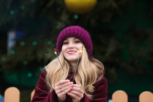 Modelo rubia emocional sosteniendo brillantes luces de Bengala en el árbol de Navidad principal en Kiev. Efecto de desenfoque