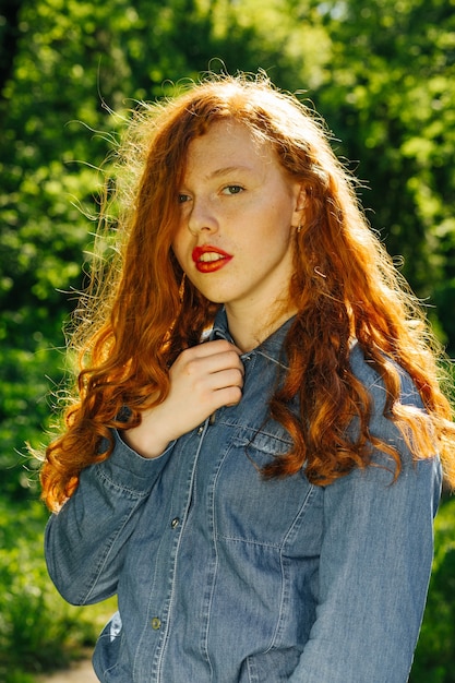 Modelo ruivo atraente com camisa jeans nos raios de sol no parque