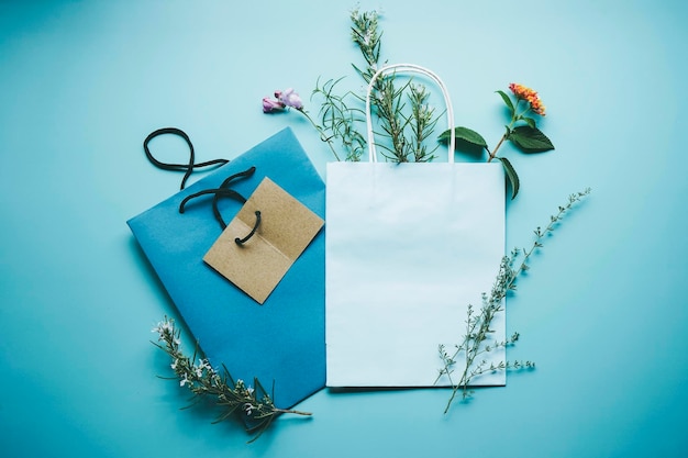 Modelo sazonal de um saco de presente de papel azul cercado por flores em formato plano