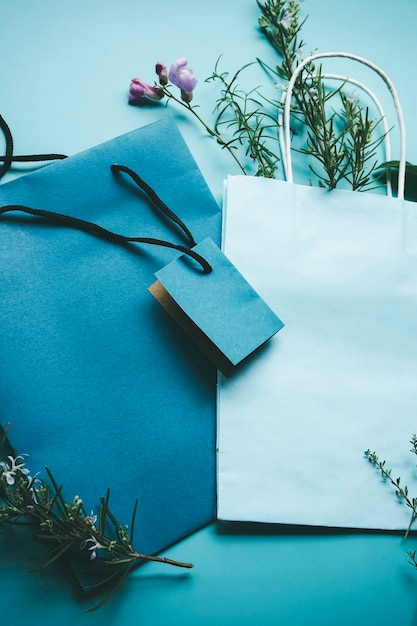 Modelo sazonal de um saco de presente de papel azul cercado por flores em formato plano