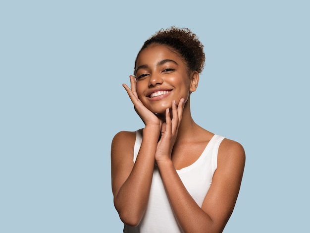 Modelo sonriente de la cara de la piel negra de la mujer de la belleza que toca su cara. Fondo de color. Azul