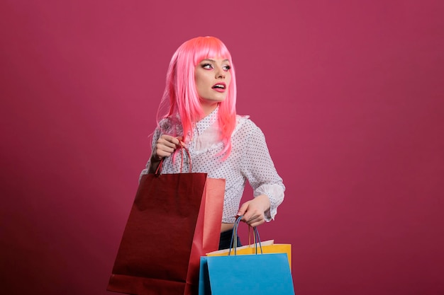 Modelo sorridente carregando sacolas coloridas de loja de varejo, usando desconto de venda no shopping para comprar roupas da moda. Segurando pacotes depois de comprar coisas elegantes, tendência de moda moderna em estúdio.