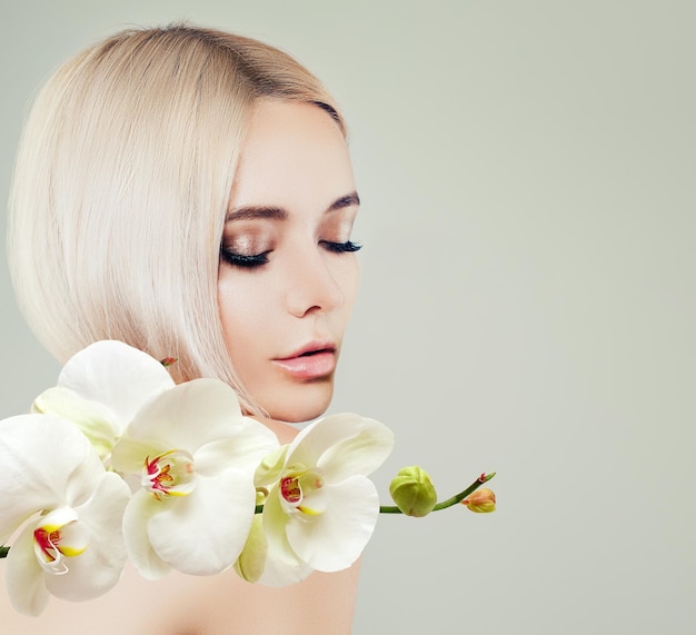 Modelo de spa de mujer linda joven con piel sana y flores de orquídeas blancas Tratamiento facial cosmetología salón de belleza cuidado de la piel y fondo de spa