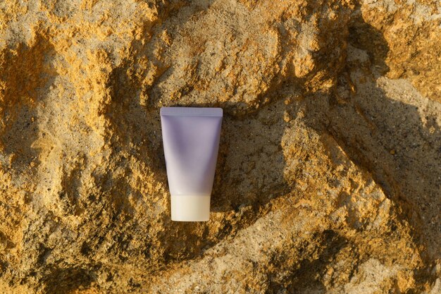 Foto modelo de tubo de crema para la piel púrpura en piedra caliza amarilla iluminada por la puesta del sol productos de belleza y concepto de cuidado de la piel