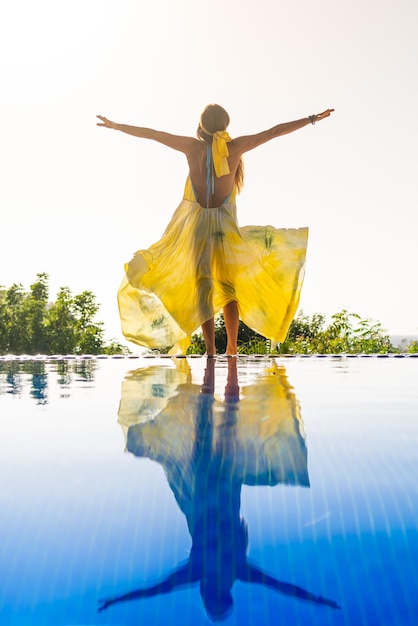 Modelo con vestido amarillo levantando los brazos en una piscina al aire libre