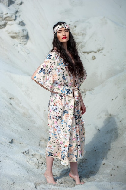 Una modelo con un vestido floral se para en la arena.