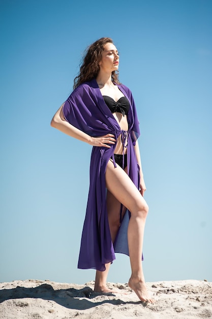 Una modelo viste una túnica morada y un bikini negro.