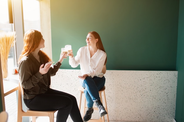 Las modelos femeninas beben café en una cafetería. Las mujeres jóvenes hablan y sonríen