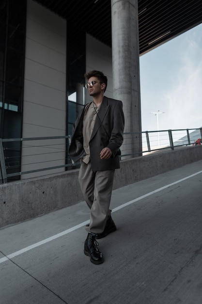 Modemann mit Sonnenbrille im stylischen grauen Anzug mit Blazer und Hemd spaziert in der Stadt