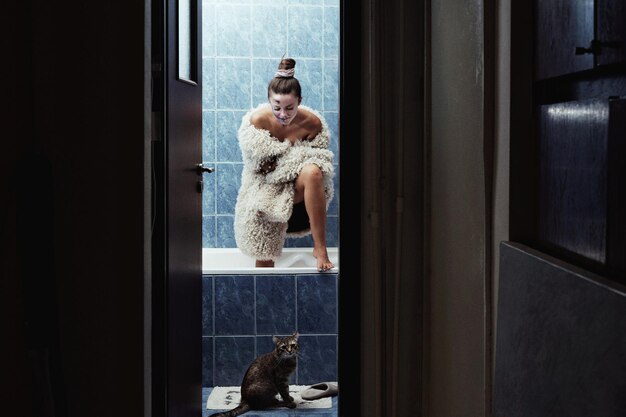 Modemodell im Kostüm steht in der Badewanne mit der Katze im Badezimmer