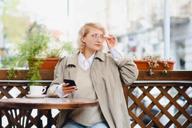 Modeporträt der jungen Frau, die am Tisch mit Tasse Kaffee, Tee im Straßencafé sitzt.