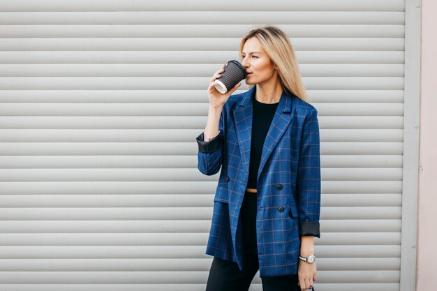 Modeporträt der jungen stilvollen Hipsterfrau, die auf der Straße geht, niedliches trendiges Outfit trägt und leckeren Kaffee trinkt