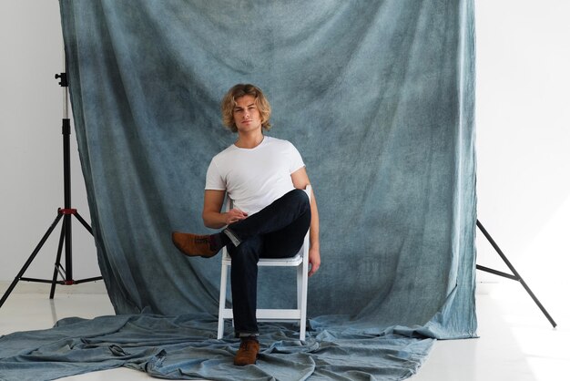 Foto modeporträt des jungen mannes im weißen hemd wirft im studio über blauem hintergrund auf