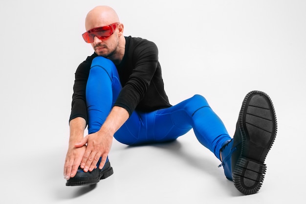 Modeporträt des stilvollen Mannes in den blauen Strumpfhosen und in den blauen Stiefeln, die sich dehnen und trainieren.