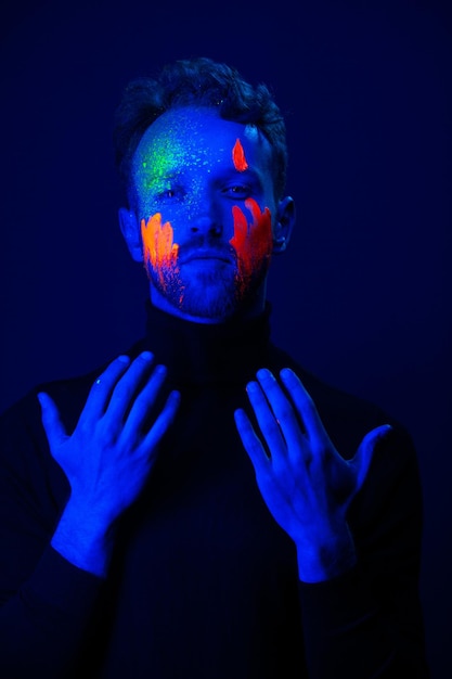 Modeporträt Ein Mann mit fluoreszierender Farbe im Gesicht unter Neonlicht