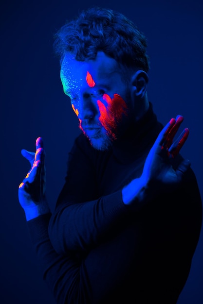 Modeporträt Ein Mann mit fluoreszierender Farbe im Gesicht unter Neonlicht