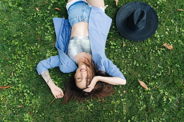 Foto modeporträt einer jungen frau, gekleidet in eine blau gestreifte jacke. frau liegt auf einem grünen rasen in einem park in der stadt