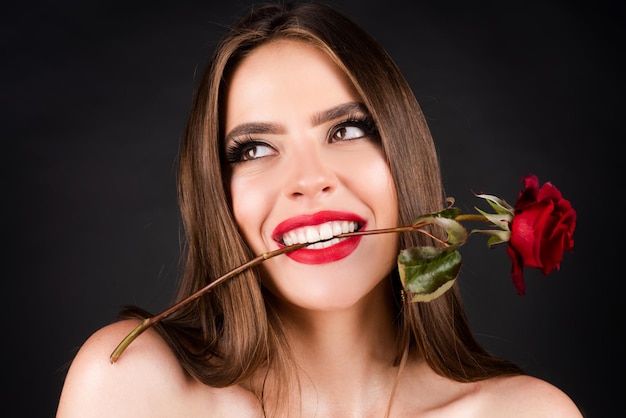 Modeporträt einer jungen schönen Frau mit roter Rose auf schwarzem Hintergrund Rosenblüten in einem Mund