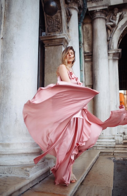 Modeporträt einer stilvollen Frau mit welligem blonden Haar im eleganten rosa Kleid Modestilkonzept
