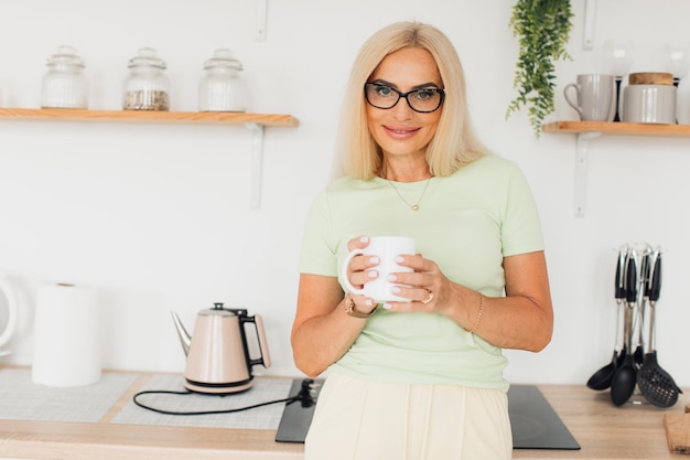 Moderna y atractiva mujer de mediana edad bebiendo café en la cocina de casa