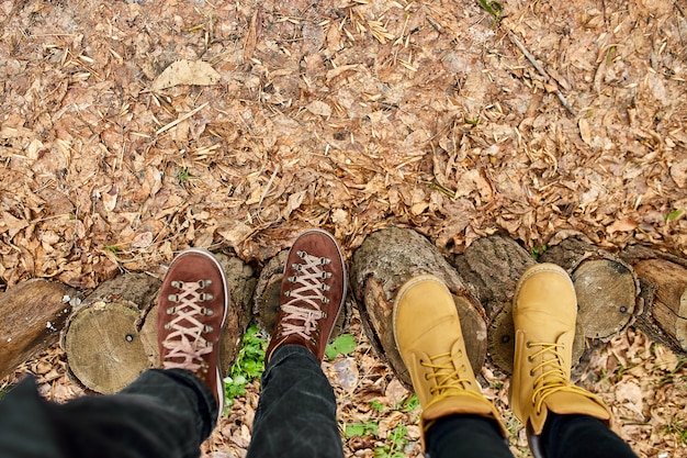 Moderna pareja joven botas de montaña en tocón de madera sobre hojas de otoño caídas en el bosque, concepto de viaje al aire libre, vista superior, amor para siempre, día de San Valentín, espacio de copia.