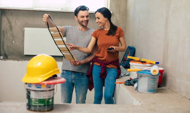 Moderna pareja joven feliz enamorada en ropa casual durante la nueva reparación o renovación de paredes con una gran cantidad de herramientas para esto