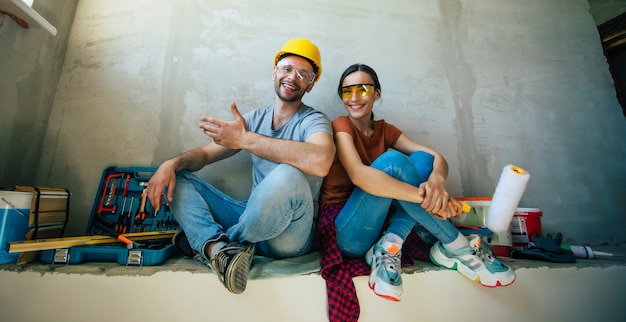 Moderna pareja joven feliz enamorada en ropa casual durante la nueva reparación o renovación de paredes con una gran cantidad de herramientas para esto